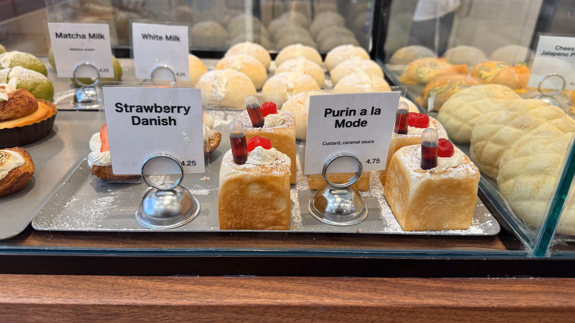 A strawberry danish topped with whipped cream and fresh strawberries beside a purin à la mode custard pastry, price tags visible.
